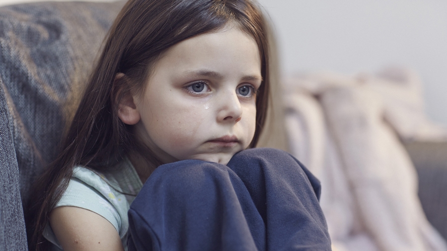 young girl crying sitting on a sofa