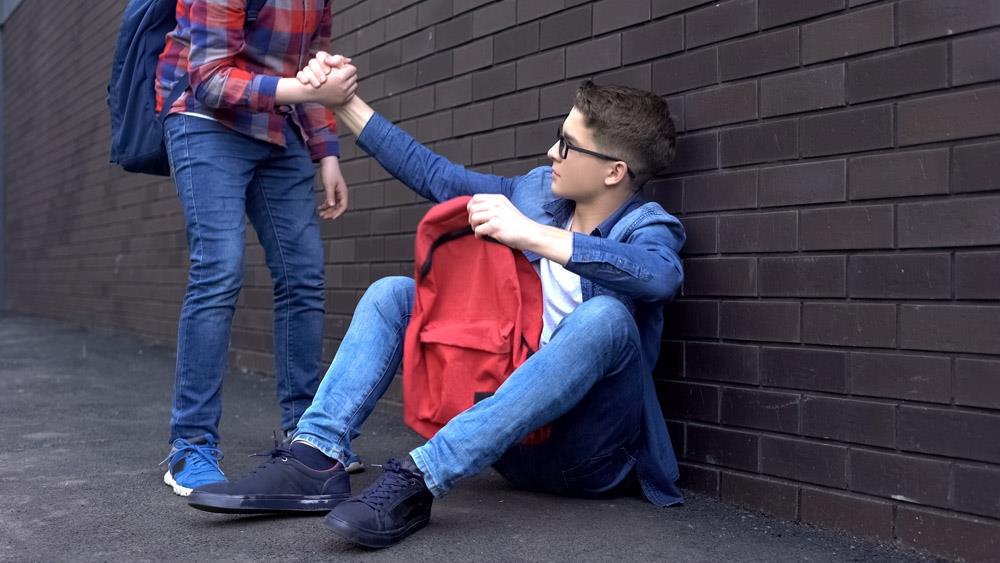 kind teenage student giving helping hand to bullied boy