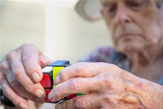 elderly man uses a cube puzzle as therapy for his diminished mental capacity due to brain damage