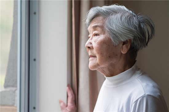 an elderly Chinese woman is feeling loneliness staring out a window