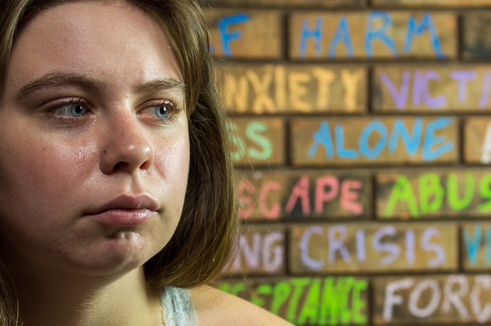 teenage girl crying in front of a brick wall background